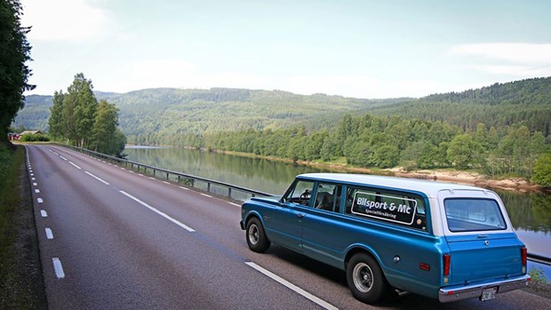 Veteranbil som åker på väg med grönska i bakgrunden